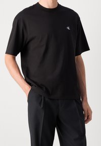 Czarna bawełniana koszulka z krótkimi rękawami i okrągłym dekoltem. Posiada małe białe logo na lewej piersi. Gładka tekstura, luźny krój.