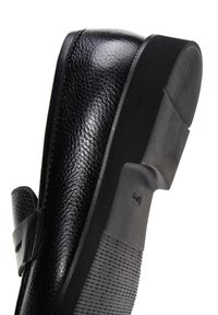 Black shoe with a textured leather upper, round toe, adjustable strap, and a flat rubber sole featuring raised grip patterns.