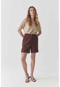 Beige short-sleeve top paired with burgundy high-waisted, cuffed shorts. The shorts feature front pockets and a button closure.