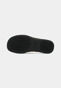 Semelle de chaussure en caoutchouc noir texturé présentant des motifs d’adhérence circulaires ressemblant à des empreintes digitales et le nom de la marque embossé au centre.