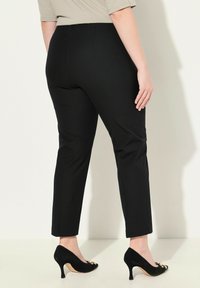 Zwarte maatpak broek met een recht gesneden ontwerp, gladde stof en een middelhoge taille, gecombineerd met zwarte hoge hakken met gouden accenten.