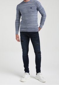 Jersey de rayas azules de manga larga con cuello acanalado, combinado con vaqueros oscuros ajustados con detalles desgastados y zapatillas blancas.