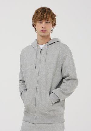 Szara bluza z kapturem, zapinana na zamek, wykonana z miękkiego materiału, z kapturem, sznurkami ściągającymi, przednimi kieszeniami oraz ściągaczami przy mankietach i na dole. Prosty, minimalistyczny design.