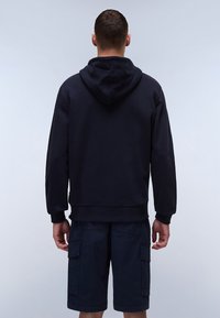 Felpa nera con cappuccio realizzata in tessuto misto cotone, con cappuccio regolabile, polsini a costine e vestibilità rilassata, abbinata a pantaloni cargo scuri.