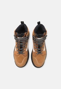 Baskets montantes en suede marron et synthétique avec des lacets noirs et blancs à motifs, semelle en caoutchouc et accents blancs contrastants.