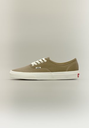 Beige Vans-sneaker met witte veters en een witte zool, van opzij gezien tegen een effen lichte achtergrond.