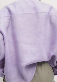 Light purple linen oversized top, featuring a relaxed shape and flowing texture, with a simple horizontal seam at the back.
