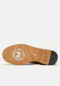 Semelle d'une chaussure en matériau liège, texturée avec des éclats multicolores, un logo circulaire et une empreinte de taille 37. Accent de talon noir lisse.