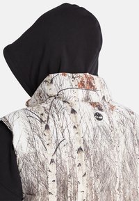 Gestepptes Weste mit einem Druck von weißen und grauen Birkenbäumen, schwarzer Kapuze und schwarzer Innenausstattung. Mit kleinem Logo auf der Rückseite.