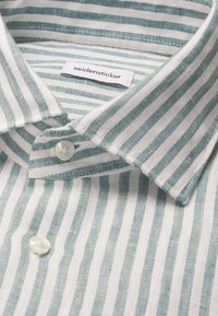 Chemise à col avec boutons, rayures verticales vertes et blanches, dotée de deux boutons blancs et d'une étiquette "seidensticker" cousue à l'intérieur du col.