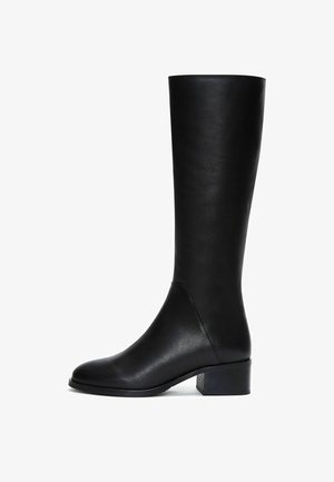 Botte noire montante en cuir lisse avec un bout légèrement arrondi, un talon bloc et un design minimaliste. Détail de couture sur le côté.