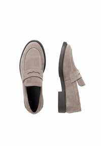 Beige suède loafers met zwarte zolen, één schoen van bovenaf getoond en de andere van de zijkant, tegen een witte achtergrond.