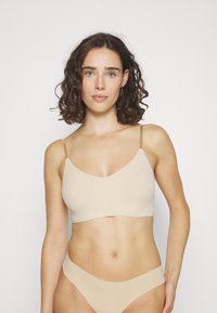 Beigefärgad bralette tillverkad av ett mjukt tyg med V-ringning och tunna remmar. De matchande trosorna har en minimalistisk design och sömlösa kanter.