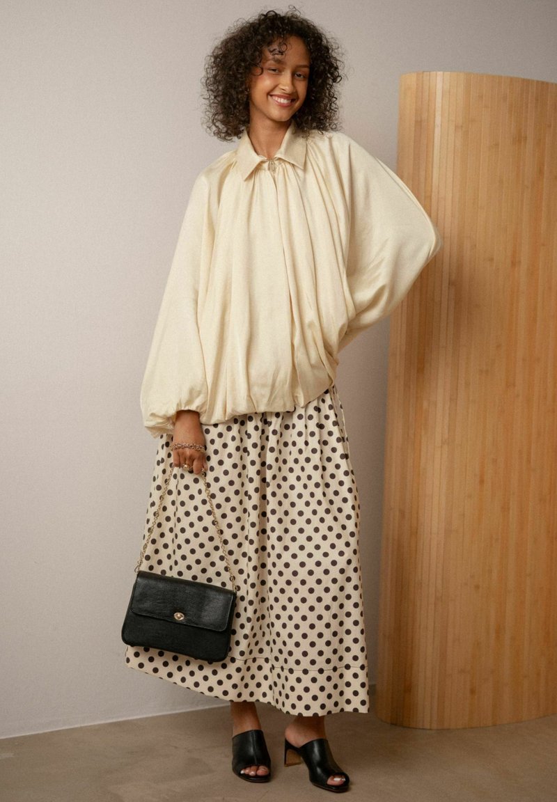 Elfenben oversized bluse med ballonærmer, polka dot midi nederdel i creme og sort, sort håndtaske med kædetræk, sorte åbne mules.