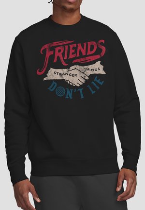 Schwarzer Pullover mit rotem, beigem und blauem Design, das zwei sich schüttelnde Hände zeigt und den Text "Friends Don’t Lie Stranger Things" enthält.