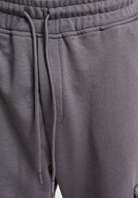 Gray cotton blend sweatpants with an elastic waistband, adjustable drawstring, and side pocket. Textured fabric with smooth finish.