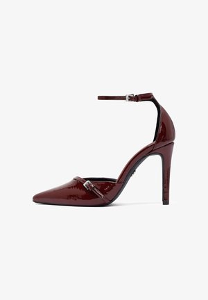 Bordeaux patent leren hoge hak schoenen met een spitse neus, enkelbandje en zilveren gesp detail. Glad textuur en slanke silhouette.