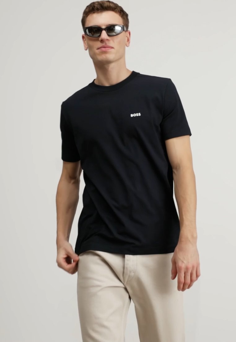 T-shirt noir à manches courtes avec un logo "BOSS" blanc sur la poitrine gauche, fabriqué en tissu doux, associé à un pantalon beige clair.