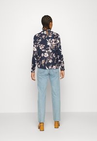 Blusa floreale a maniche lunghe in blu navy con fiori crema e rosa, abbinata a jeans blu chiaro e scarpe con tacco a blocco marroni. Vestibilità standard.