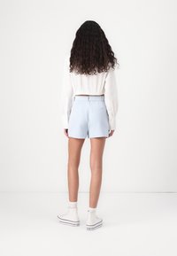 Pantaloni corti azzurri chiari con vita aderente e due tasche posteriori, abbinati a una maglietta bianca a maniche lunghe e a un paio di sneaker bianche alte.