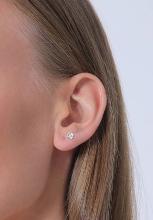 Boucle d'oreille en argent rond avec un cristal transparent. Gros plan de l'oreille, mettant en valeur une peau lisse et des cheveux bruns raides.