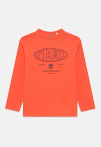 Hosszú ujjú narancssárga póló "Timberland" felirattal, egy fa logóval, valamint az "Első osztályú minőség" és a "Robusztus Aktív Felszerelés" feliratokkal az elején.