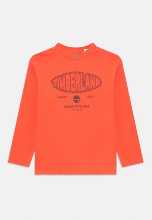Maglietta arancione a maniche lunghe con il testo "Timberland", un logo ad albero e le frasi "Qualità Superiore" e "Abbigliamento Attivo Robusto" sul davanti.