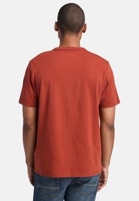 Rust red cotton t-shirt with short sleeves, a crew neckline, and a simple design, featuring a straight hem and no visible logos.