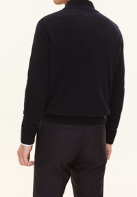 Pull en tricot navy avec un col montant, des bords côtes en bas et aux poignets, une texture lisse et une coupe décontractée, porté sur un pantalon sombre.