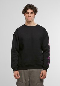 Sort sweatshirt med rund halsudskæring, oversized pasform og lilla palmetræ-grafik på venstre ærme. Glat stof struktur.