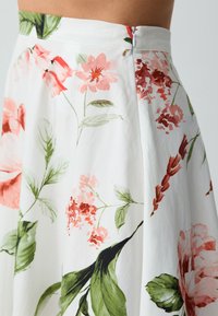 Blumiger Rock aus weißem Stoff mit rosa und grünen Blumenmustern, mit einem enganliegenden Taillenbund und einem Reißverschluss auf der Rückseite.