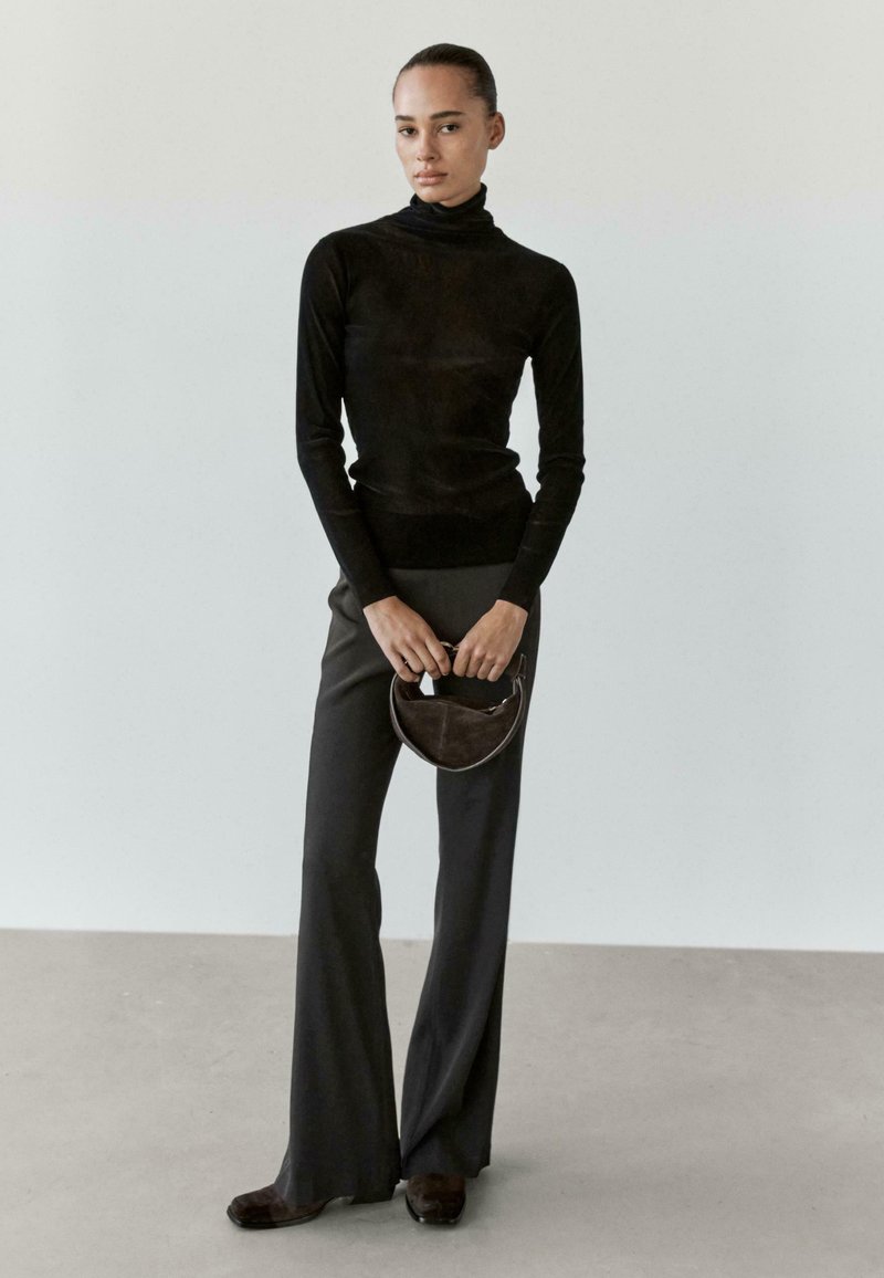 Czarny sweter z golfem połączony z luźnymi czarnymi spodniami i ciemnymi butami. Trzyma małą, zakrzywioną brązową torebkę. Prosty i minimalistyczny design.