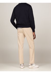 Felpa blu navy con polsini a costine, pantaloni chino beige con vestibilità dritta e scarpe bianche con dettagli neri e rossi.