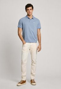 Světle modré polo tričko s krátkým rukávem a vzorem puntíků; spárované s krémovými kalhotami a hnědými teniskami. Ležérní střih.