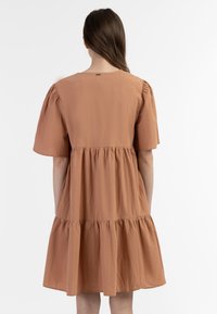 Brun kortærmet kjole med løs pasform, lagdelte flæser ved kanten og blød tekstur, der har en subtil detalje med et bagtag.
