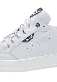 Baskets en cuir blanc avec des détails perforés, accents noirs et lacets texturés. Comprend une semelle blanche plate et un col rembourré pour le confort.