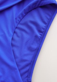 Zbliżenie na jasnoniebieską, elastyczną tkaninę z wyraźnym szwem, ukazujące fakturę i zakrzywiony szew na jasnym tle.