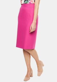 Fuksjowa spódnica ołówkowa o gładkiej fakturze, z wysokim stanem i dyskretną kieszenią boczną. Połączona z jasnobeżowymi butami na słupku.