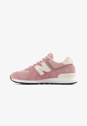 Różowy zamszowy i siateczkowy sneaker z białymi sznurowadłami, kremowym logo „N” i białą amortyzowaną podeszwą z czarną nakrapianą spodem.