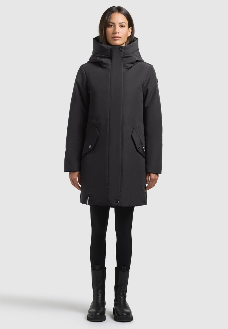 Mustast pehmendatud parka kõrge kraega, ees oleva nööpidega sulgemise ja kahe suure küljetaskuga. Materjal tundub sile ja veekindel.