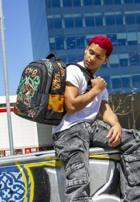 Mochila negra con gráficos en estilo graffiti naranjas, una figura patinando y un bolsillo lateral de malla. Cuenta con correas acolchadas y una forma redondeada.