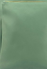 Groene leren zip-pocket met textuur, voorzien van een gladde afwerking en gouden ritsdetails. Compacter ontwerp, ideaal voor kleine items.
