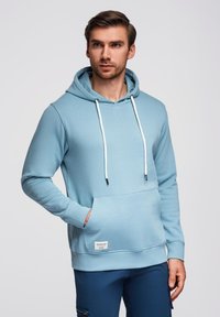 Felpa leggera blu chiaro realizzata in tessuto morbido, dotata di tasca frontale, cappuccio con stringa e stringhe bianche a contrasto.