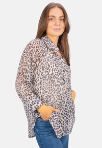 Sheer button-up shirt in gray with black leopard print, featuring a collar, long sleeves, and two front pockets. Worn with blue jeans.
