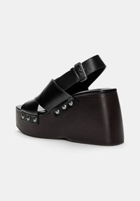 Crne platforme sandal s kožom, širokim remenom, podesivom kopčom na gležnju i teksturiranim tamnosmeškim klinastim potplatom koji ima dekorativne klinčiće.