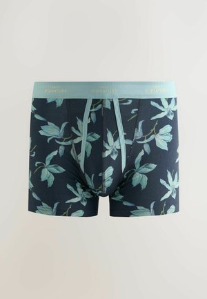 Boxers tipo bóxer en color azul marino con un patrón de hojas en azul claro y verde. Cuenta con una cinturilla azul clara con el texto en dorado "NEXT SIGNATURE".