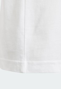 Camiseta de algodón blanca con dobladillo de terminación limpia y costura lateral. El material es suave y texturizado, con un corte clásico. Sin patrones ni acentos.