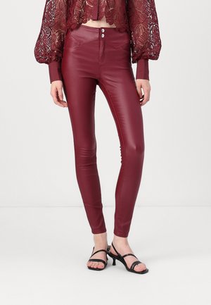 Pantalons skinny en simili cuir bordeaux avec une taille haute, dotés de deux poches avant et d'une fermeture à bouton en haut. Texture lisse et ajustée.