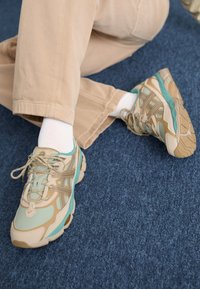 Scarpe sportive con una combinazione di colori verde menta, beige e marrone. Presentano pannelli in rete e suole spesse con battistrada decorato. Texture morbida.
