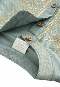 Chemise en tissu bleu clair ornée de broderies dorées complexes, avec des boutons et un motif texturé. L'étiquette indique "NEXT Baby, fabriqué en Inde."
